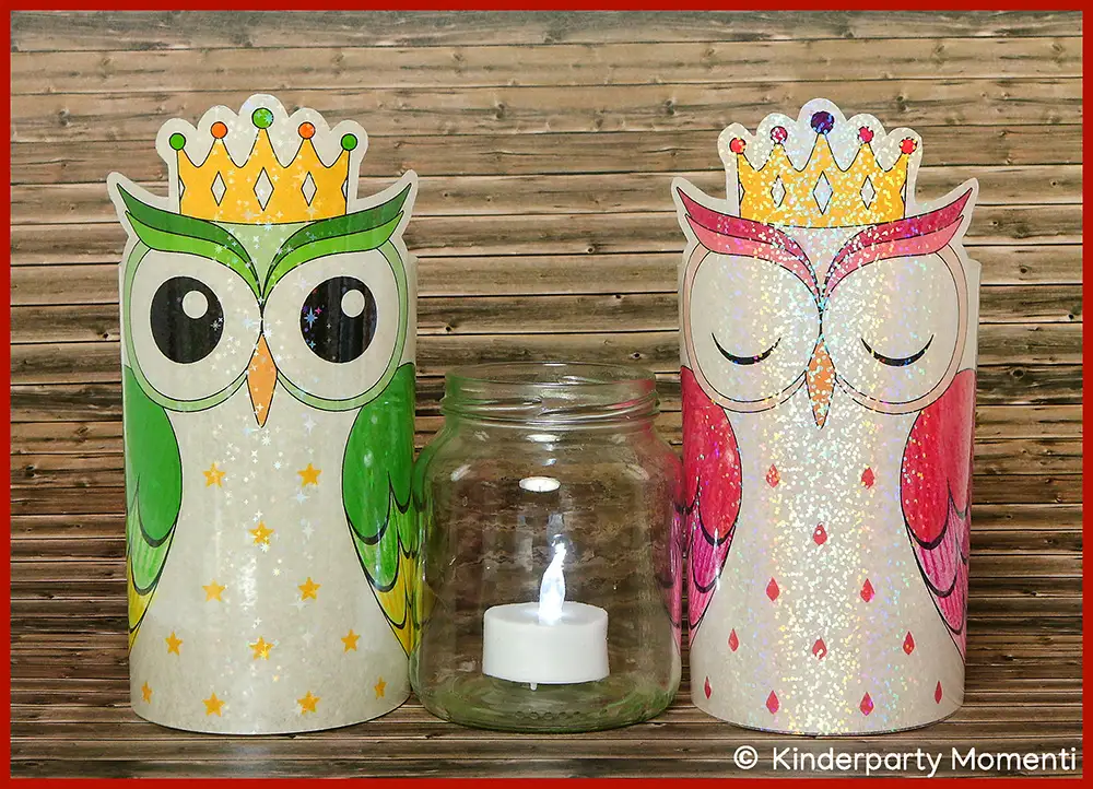 Zwei mit holographischer Folie beklebte DIY Eulen Windlichter mit Kronen, eine grün und eine rosa, flankieren ein Glas mit einer brennenden Teelichtkerze vor Holzwand.