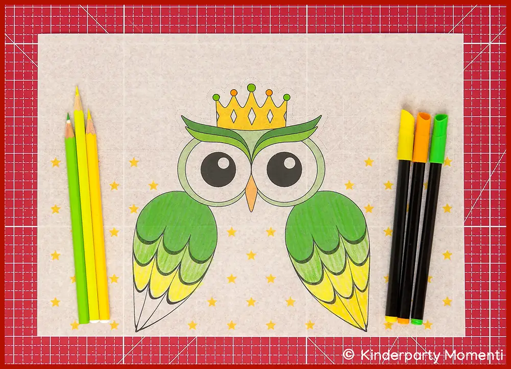 Bunte Zeichnung einer Eule mit Krone, umgeben von gelben Sternen, daneben liegen gelbe und grüne Buntstifte auf rotem Schneideunterlage.
