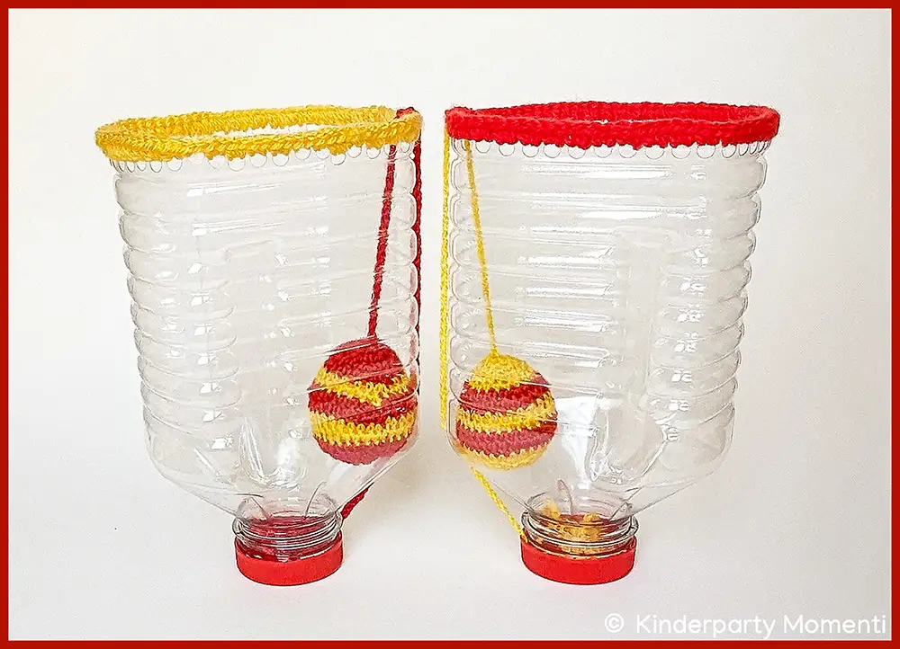 Idee für Oster DIY Spiele - Fangbecher basteln aus großer Plastikflasche mit Osterei als Ball Zwei aus durchsichtigen Plastikflaschen gebastelte Fangbecher Spiele mit gehäkelten rot-gelb gestreiften Ostereiern als Ball