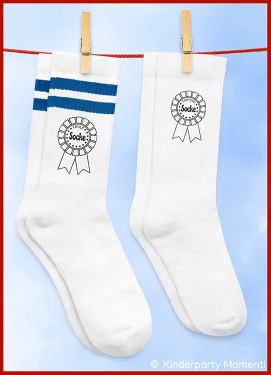 Zwei weiße Socken an einer Wäscheleine, eine mit blauen Streifen und beide mit einem Aufdruck einer Siegermedaille und dem Wort 'Faule Socke' und 'Tapfere Socke'