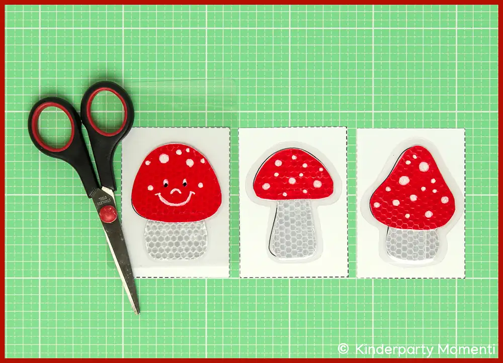 Drei rote Fliegenpilz mit weißen Punkten auf grüner Bastelmatte neben schwarzer Schere.