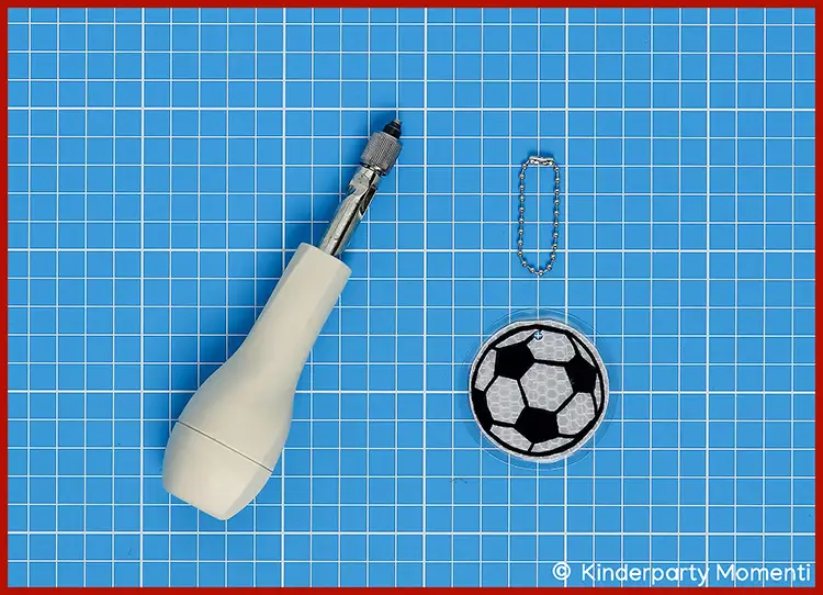 Fußball-Anhänger mit Kugelkette neben einem weißen Handbohrer auf Bastelmatte
