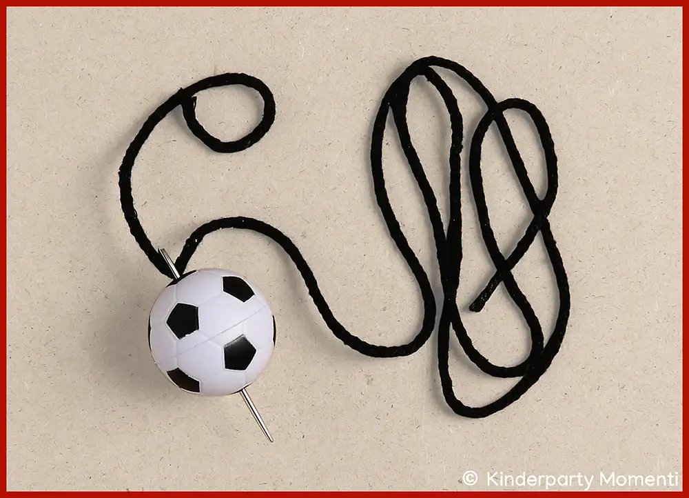 Ein schwarzes Band eingefädelt in eine Nadel steckt in einem kleinen Fußball