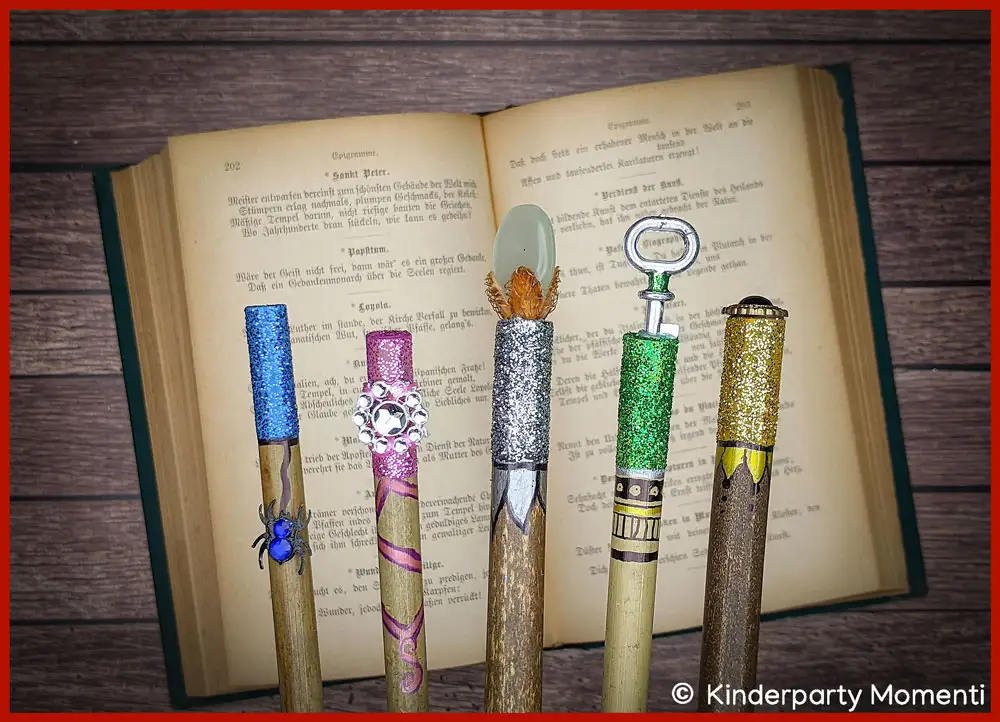 Hexen Zauberstäbe basteln mit Glitzer-Steinen & Glitter Fünf bunte DIY Zauberstäbe mit Glitzer-Verzierungen liegen auf einem aufgeschlagenen alten Buch.