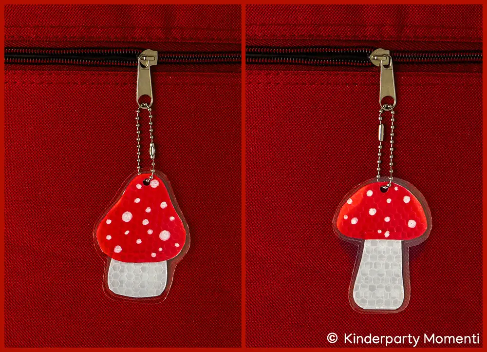 Zwei Reflektierende Fliegenpilz Anhänger sind an einem Reißverschluss einer roten Tasche befestigt.