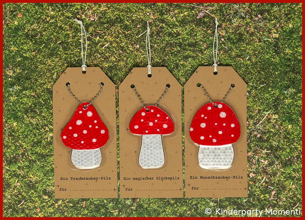 Drei gebastelte Fliegenpilz Anhänger mit roten Kappen und weißen Punkten auf braunen Geschenkanhängern, liegend auf grünem Moos.