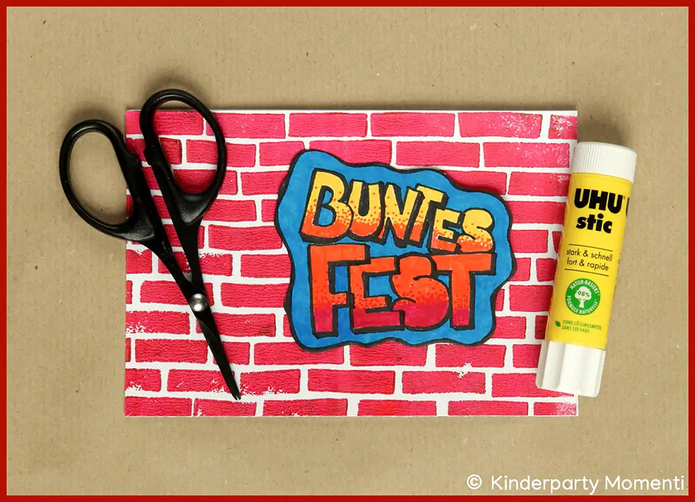 Vorlage für eine Weihnachtskarte mit rotem Ziegelmuster und Schriftzug 'BUNTES FEST', daneben schwarze Schere und gelber UHU-Stift.
