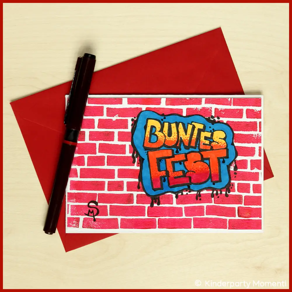 Handgemachte Weihnachtskarte mit roter Backsteinmauer und Graffiti-Schriftzug 'BUNTES FEST' in Blau, Gelb und Rot, daneben roter Umschlag und schwarzer Stift.