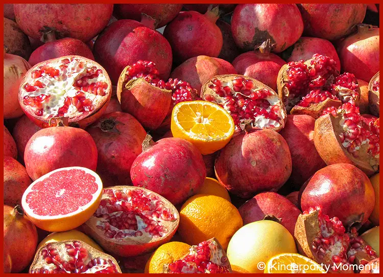 Marktstandauslage mit Granatäpfeln und Orangen Mehrere ganze und aufgeschnittene Granatäpfel sowie eine aufgeschnittene Orange und eine ganze Orange liegen dicht beieinander