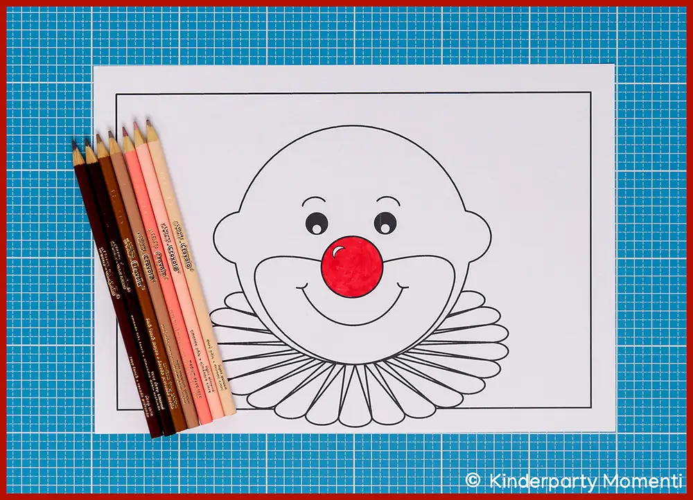 Ausgemaltes Clownsgesicht mit roter Nase auf Papier neben einer Gruppe Hautfarbstiften in verschiedenen Tönen auf blauem Untergrund