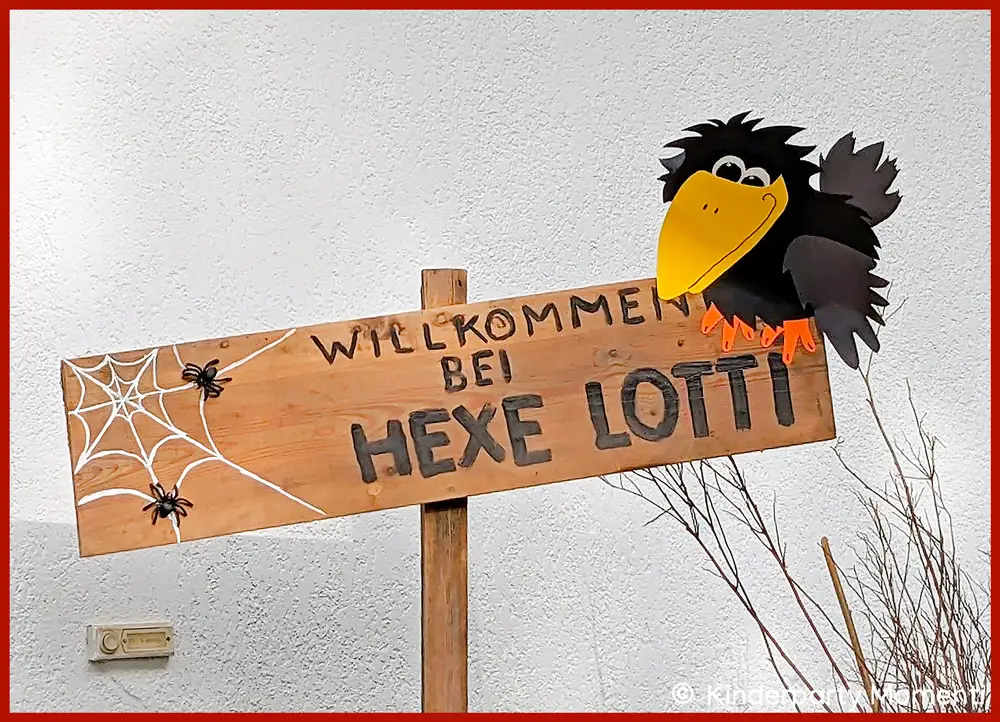 Willkommen-Schild zur Hexenparty Holzschild zur Begrüßung beim Kindergeburtstag mit der Aufschrift 'WILLKOMMEN BEI HEXE LOTTI', verziert mit zwei Spinnen in einem Spinnennetz und einer schwarzen Rabenfigur mit gelbem Schnabel.
