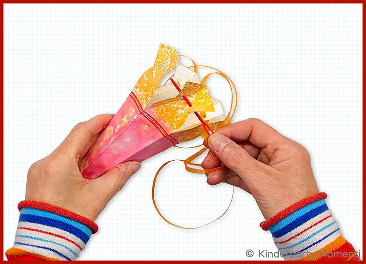 Hände fädeln mit einer Nadel eine Schnur um eine kleine bunte Zuckertüte
