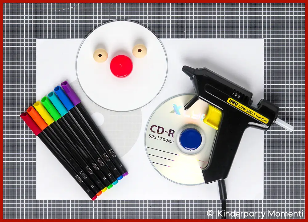 Bastelmaterial für DIY Kreisel aus CDs Bastelmaterialien auf weißem Papier mit zwei CDs, bunten Filzstiften, Holzperlen und einer Heißklebepistole