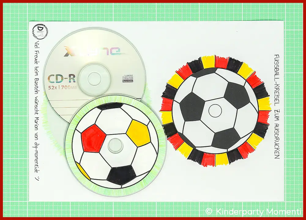 Ausgemalte CD Etiketten auf alte CDs kleben Zwei CDs mit schwarz-weißen Fußballmustern, eine davon mit rot-gelb-schwarzen Markierungen, daneben eine farbige Zeichnung eines Fußball-Kreises mit denselben Farben auf grüner Bastelmatte
