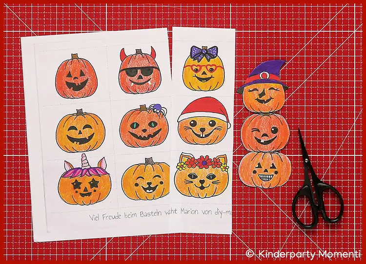 Zwei ausgedruckte Bastelvorlagen mit bunt ausgemalten Kürbisgesichtern in verschiedenen Halloween-Motiven auf roter Schneidematte