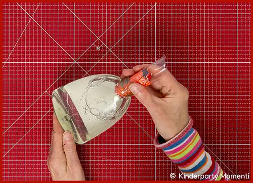 Hände schieben ein selbstgemaltes Kürbisbild in eine Seifenspender Flasche - Hintergrund rote Bastelmatte