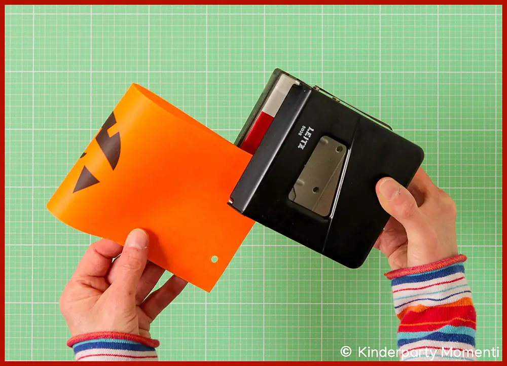 Hände halten lochen orangefarbenes Windlicht aus Transparentpapier mit einem schwarzen Locher