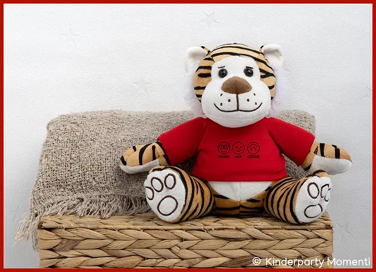 Kuscheltier Tiger als Geschenk zur EInschulung Plüsch-Tiger mit rotem T-Shirt sitzt auf geflochtenem Korb vor weißer Wand