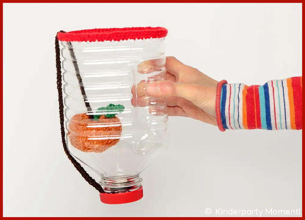 DIY Fangbecher Spiele aus Plastikflaschen basteln Hand hält ein Fangbecherspiel aus einer durchsichtigen Plastikflaschel, darin ein gehäkelter Kürbis, an einer Schnur befestigt.