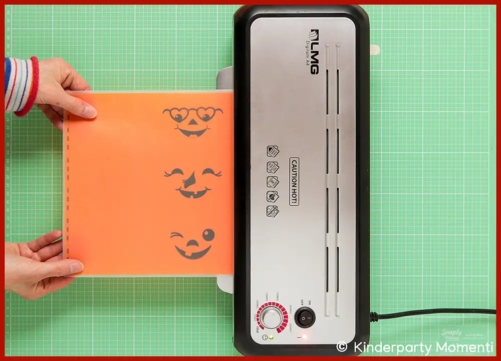 Halloween Vorlagen für Flaschenetikett Banderole durch laminieren stabilisieren Hände führen orangefarbene Flaschenetikett Voralge mit drei lachenden Kürbisgesichtern in Laminiergerät ein