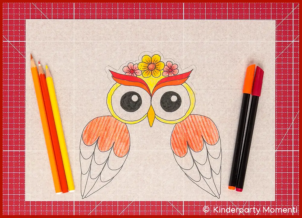 Bunte Zeichnung einer Eule mit Blumen-Krone, daneben liegen gelbe und orangene Buntstifte und Filzstifte, die Vorlage zum Basteln der Eulen Laterne liegt auf einer roten Bastelmatte