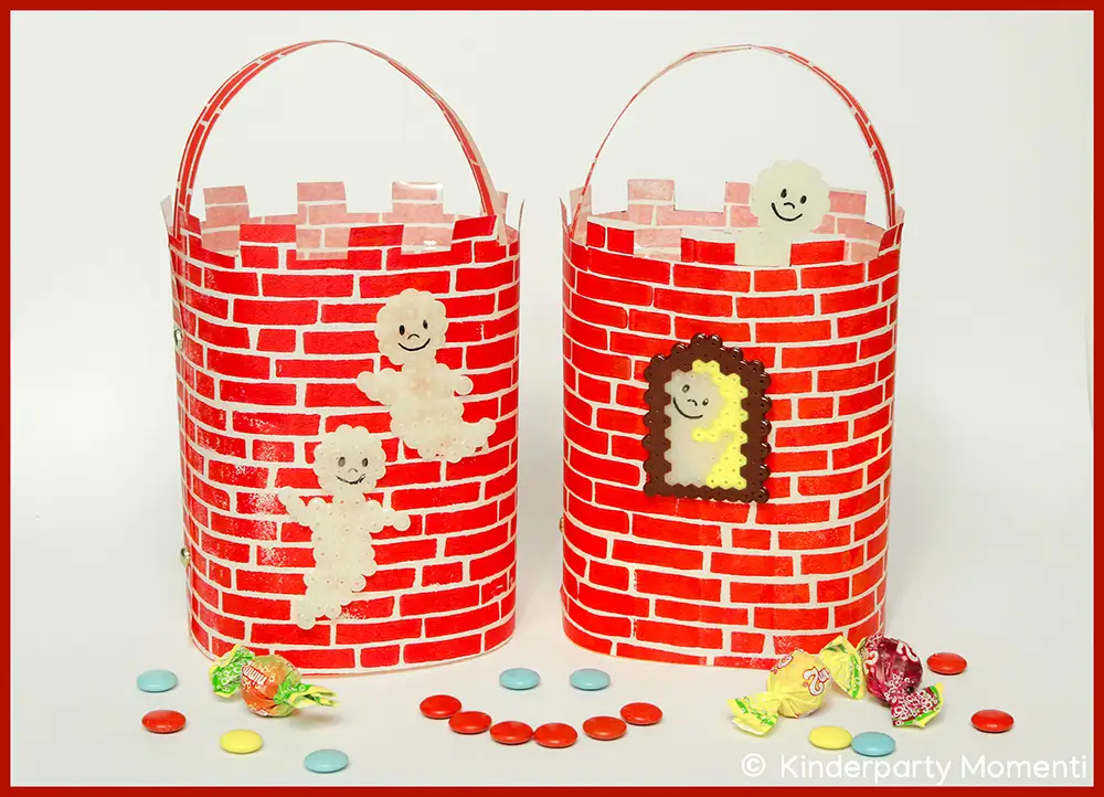 Zwei Laternen aus rotem Papier mit Backsteinmuster, verziert mit lachenden Bügelperlen Gespenstern, umgeben von bunten Bonbons.