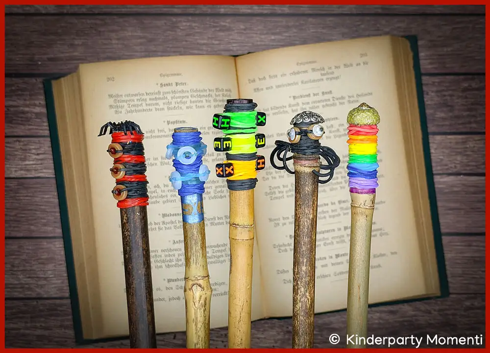 Hexen Zauberstäbe basteln mit Loom Gummis und Perlen Fünf bunte DIY Zauberstäbe, die oben mit Loom Gummibändern und Perlen umwickelt sind, liegen auf einem alten aufgeschlagenen Buch.