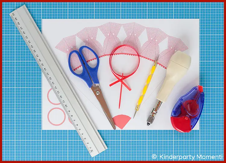 Kleine Schultüten selber basteln - Vorlagen & Material Bastelmaterialien für eine Schultüte auf blauem Schneideunterlage mit Lineal, Schere, Kleberoller, Locher, Bleistift und Papier mit Schultütenmuster