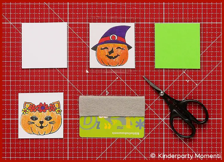 Zwei ausgedruckte Bastelvorlagen mit bunt ausgemalten Kürbisgesichtern in verschiedenen Halloween-Motiven auf Memo Spielkarten geklebt - Untergrund rote Schneidematte