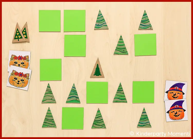 Mehrere grüne quadratische und dreieckige Memo Spielkarten mit Weihnachtsbaum-Motiven sowie Karten mit Kürbisgesichtern auf hellem Holzhintergrund