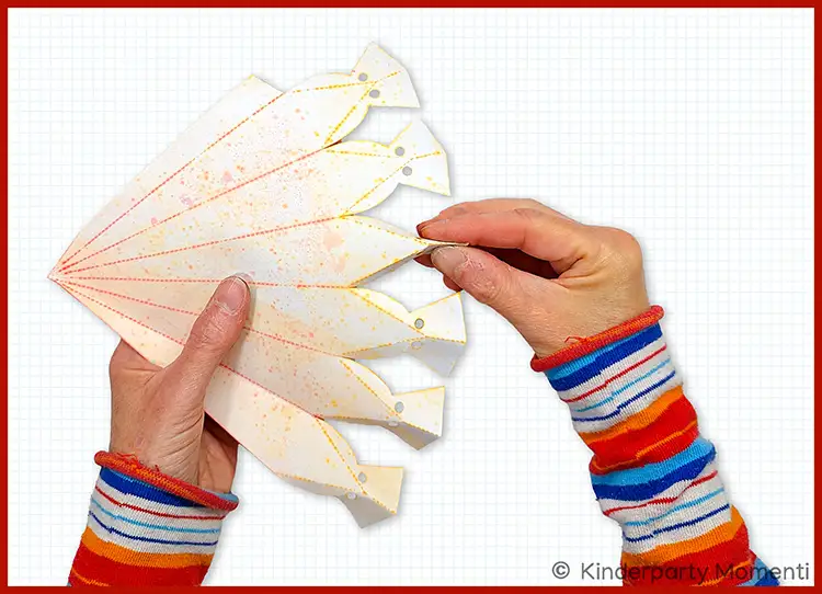 Hände falten eine Schultüte aus Papier mit vorgezeichneten Linien auf kariertem Hintergrund