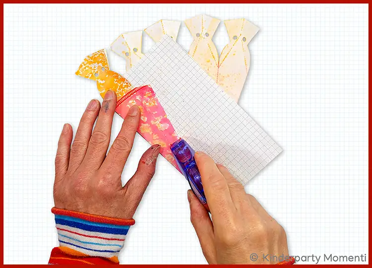 Hände betreichen eine kleine bunte Schultüte aus Papier mit einem Rollkleber