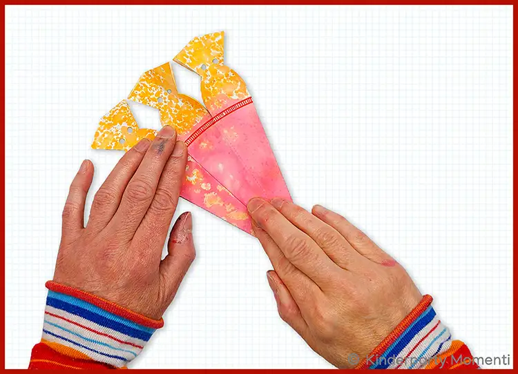 Hände kleben eine kleine Schultüte aus pinkem und gelbem Papier mit Mustern zusammen