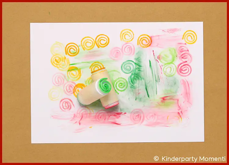 Mehrfarbige Spiralmuster auf weißem Papier mit zwei Moosgummistempeln in der Mitte