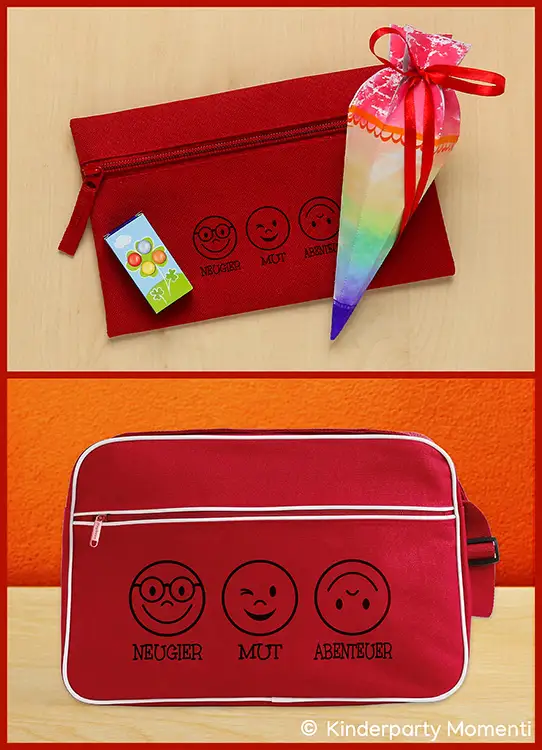 Rotes Federmäppchen mit drei schwarzen Smiley-Gesichtern und den Worten 'Neugier Mut Abenteuer' daneben eine bunte Schultüte und ein kleines Päckchen sowie rote Retro-Tasche mit weißen Paspeln und denselben drei Smileys und Worten vor orangefarbener Wand