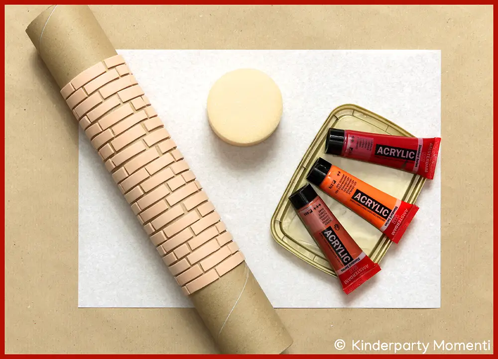 DIY Moosgummi Stempel Rolle mit Ziegelsteine Muster, runder Schwamm und drei Acrylfarben in Rot-, Orange- und Braun-Tönen auf weißem Papier.