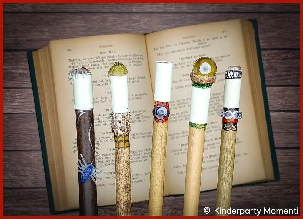 Nachleuchtende Hexen Zauberstäbe basteln mit Kindern Fünf, mit nachleuchtendem Klebeband dekorierte, DIY Zauberstäbe liegen auf einem aufgeschlagenen Buch