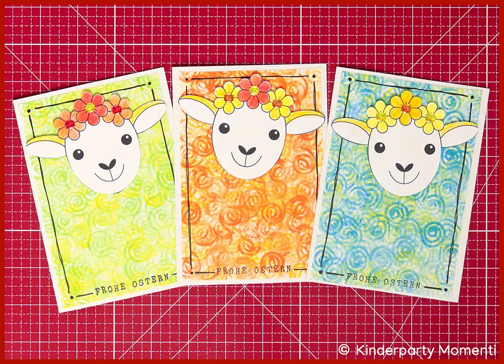 Schäfchen Osterkarte selber machen Drei bunte Osterkarten mit Schafgesichtern mit Blumenkränzen auf gemustertem Hintergrund, darunter der Schriftzug 'FROHE OSTERN'