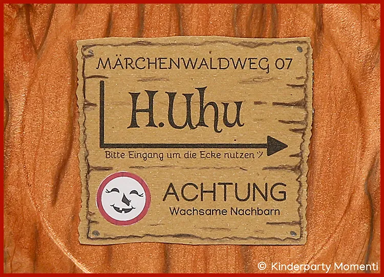 Holzschild mit der Aufschrift 'MÄRCHENWALDWEG 07 H. Uhu Bitte Eingang um die Ecke nutzen' und darunter 'ACHTUNG Wachsame Nachbarn' mit einem Symbol aus drei lachenden Monden in einem roten Kreis