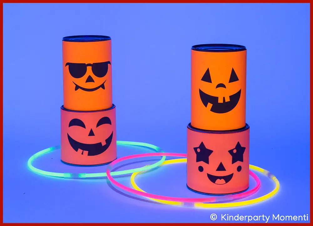DIY Spiele Ideen für Kindergeburtstag im Schwarzlicht - Ringe werfen mit Knicklichter Ringen Jeweils zwei mit Neon-Papier beklebte Dosen mit Halloween-Gesichtern stehen übereinander, drumherum liegen drei Knicklichter Ringe, die im Schwarzlicht leuchten