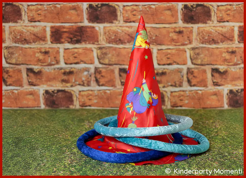 Ideen für Hexen Kindergeburtstag - Hexenhut - Pylone für Ringe werfen Spiel verwenden DIY Ringe Werfen Spiel aus Pylone mit rotem Hexenhut mit bunten Sternen und Hexenmotiv, drumherum drei blaue Ringen, vor Ziegelsteinwand auf grünem Untergrund