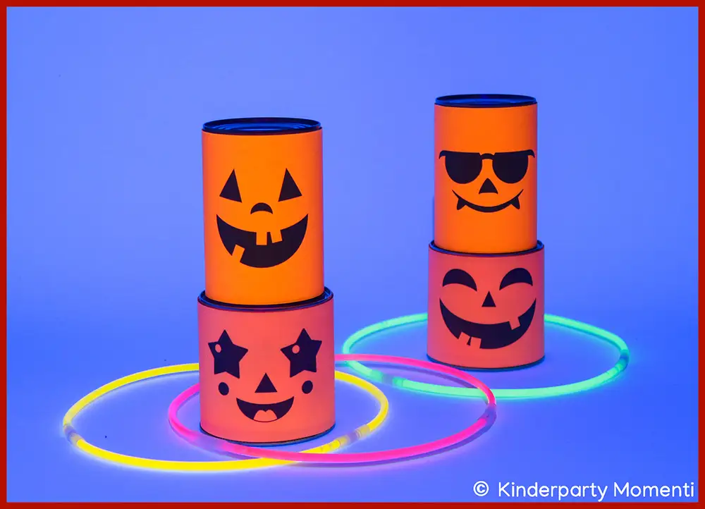 DIY Kindergeburtstag Spiel - Ringe werfen mit Wurfringen aus Knicklichtern Jeweils zwei mit Neon-Papier beklebte Dosen mit Halloween-Gesichtern stehen übereinander, drumherum liegen drei Ringe aus Knicklichtern, die im Schwarzlicht leuchten