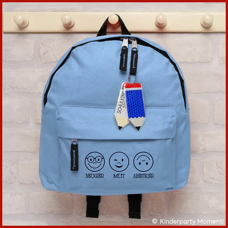Hellblauer Rucksack mit drei aufgedruckten Emoticons und den Worten Neugier, Mut, Abenteuer sowie zwei Anhängern in Stiftform