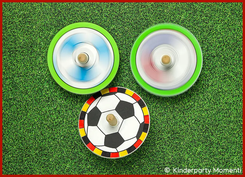 Selbstgebastelte Fußball Spielzeug Kreisel aus CDs Drei selbstgebastelte Kreisel mit Fußball- und Farbmuster auf grünem Rasen Hintergrund