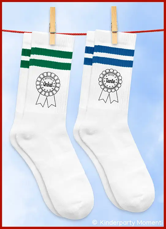 Zwei weiße Socken mit grünen beziehungsweise blauen Streifen und Aufdrucken in Form von Schleifen mit den Worten 'Bester Onkel!' und 'Beste Tante'