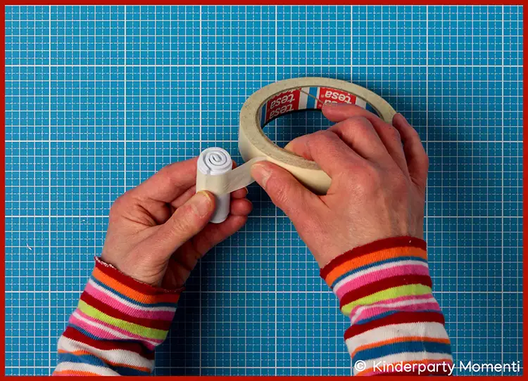 Hände mit bunt gestreiftem Langarmshirt umkleben Moosgummi Stempel mit Klebeband auf einem blauen Schneideunterlage mit weißem Raster