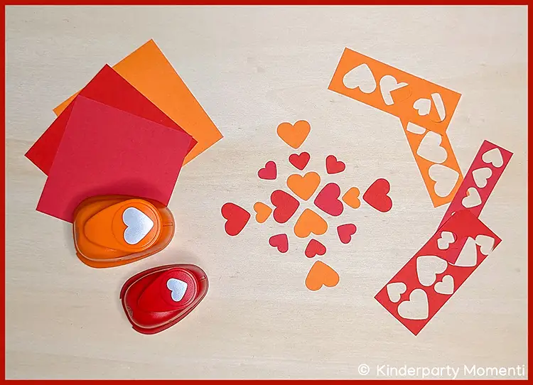 Aus buntem Papier Herzen mit Motiv Stanzer ausstanzen Zwei Herz-Motivstanzer mit ausgeschnittenen Herzformen und buntem Papier auf hellem Untergrund