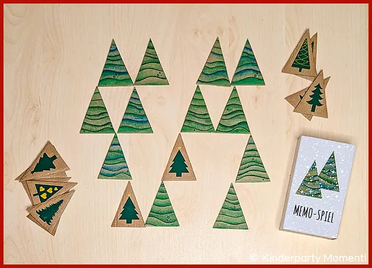 Mehrere Memo Spielkarten mit Tannenbaum-Motiven liegen auf einem hellen Holztisch, daneben eine Streichholzschachtel mit aufgeklebten Tannenbäumen