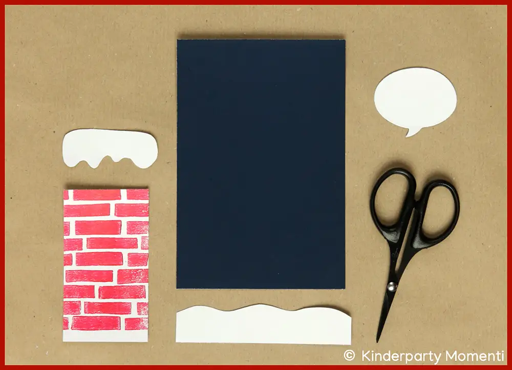 Schwarze Schere neben ausgeschnittenen Elementen für eine Weihnachtskarte - eine Sprechblase, kleine Schneeberge sowie einem Rechteck mit rotem Ziegelmuster auf braunem Untergrund.