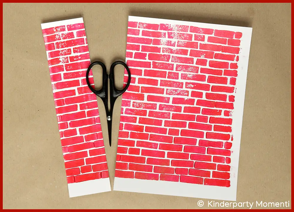 Schwarze Schere liegt zwischen zwei Papierstücken mit rotem Backsteinmuster auf braunem Untergrund.